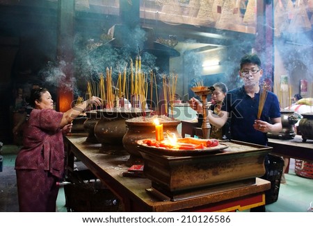HO CHI MINH CITY, VIETNAM- AUG 10 : People burn incense at ancient temple, incense stick in censer, smoke spriral, this traditional culture of buddhism religion, woman in solemn, Vietnam, Aug 10, 2014