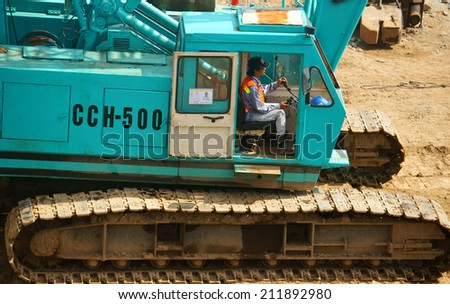 HO CHI MINH, VIETNAM- AUG 9: People control excavator at construction site, man sitting on cabin to drive, wheel of machine is chain, moving on land, Vietnam, Aug 9, 2014