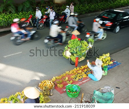 HO CHI MINH, VIETNAM- AUG 18: Immigrant woman earn money by banana street vendor, bike fiilled with bunch of bananas, other people selll on pavement, motorbike move blur on road, Vietnam, Aug 18, 2014