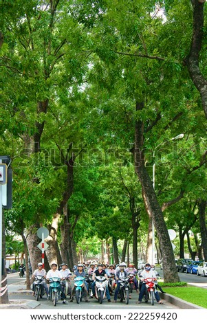 HO CHI MINH CITY, VIET NAM- OCT 7: Fresh air at Asian city, row of big tree on street, group of Vietnamese people on motorbike stop on street, ancient green trees with big trunk, Vietnam, Oct 7, 2014