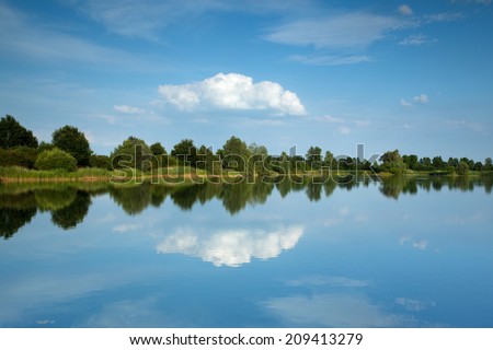 Lake with trees, clouds and light blue sky reflected in water