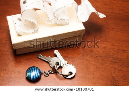 Two keys lying next to a cream colored gift box