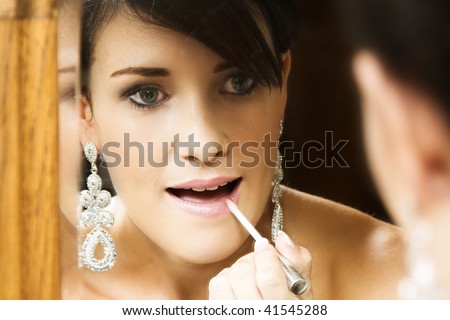 Beautiful brunette bride applying lip-gloss in the mirror