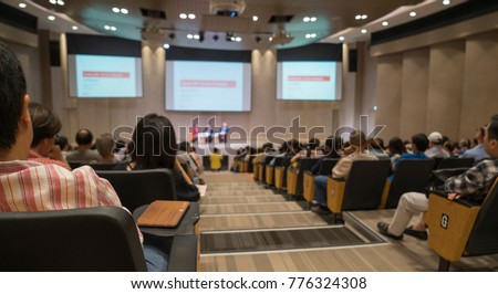 Audience view, speaker speech on stage with LED projector screen. Business conference presentation in hall, seminar meeting room.  People listening talk show.  Education  and business concept