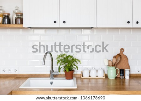 View on white kitchen in scandinavian style, kitchen details, plants on wooden table, white ceramic brick wall background