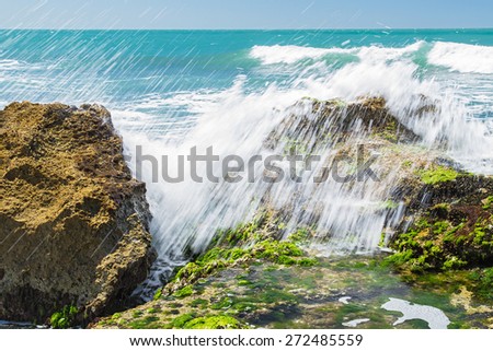 Turquoise rolling wave slamming on the rocks of the coastline