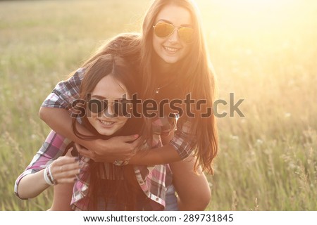 Two playful young women having fun outdoors at sunset light. Strong sun glare