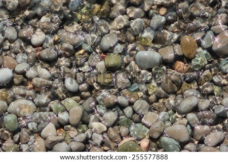 Sea pebbles in water. Ripples on the surface of water and solar patches of light.