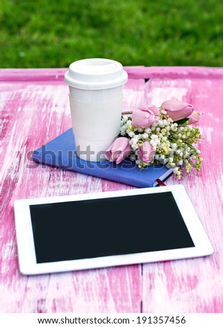 diary, a tablet computer, a glass of coffee and  lilies of valley and tulips on the table