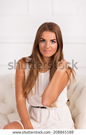 young blond beautiful girl in white dress sitting on a white couch