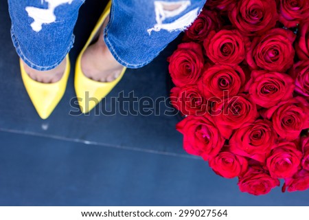 The bouquet of red roses and female legs in jeans and yellow shoes with heels. View from above.