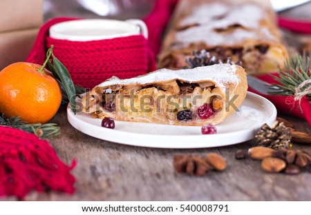 strudel and winter decor. Christmas homemade pastry. Apple strudel (pie) with dried fruits, oranges, cranberries, walnuts and powdered sugar with Christmas decor close up. Winter decor. Rustic style.
