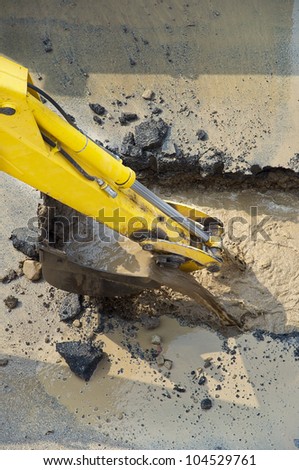 excavator digging a hole, breaking street asphalt, repairing damaged water supply