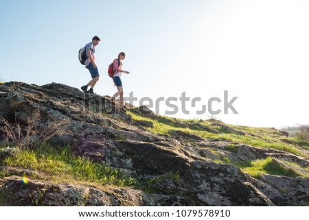 Couple of Young Happy Travelers Hiking with Backpacks on the Beautiful Rocky Trail at Warm Sunny Evening. Family Travel and Adventure Concept.