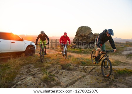 Friends Cyclists Riding Enduro Bikes in the Mountains in front of the Pickup Off Road Truck at Warm Autumn Sunset. MTB Adventure and Car Travel Concept.