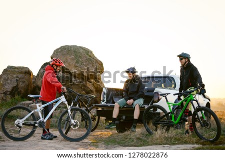 Friends Cyclists Resting near the Pickup Off Road Truck after Enduro Bike Riding in the Mountains at Warm Autumn Sunset. MTB Adventure and Car Travel Concept.