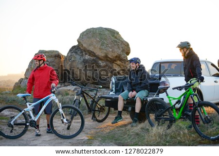 Friends Cyclists Resting near the Pickup Off Road Truck after Enduro Bike Riding in the Mountains at Warm Autumn Sunset. MTB Adventure and Car Travel Concept.