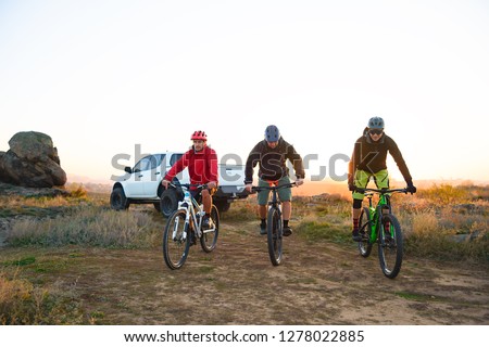 Friends Cyclists Riding Enduro Bikes in the Mountains in front of the Pickup Off Road Truck at Warm Autumn Sunset. MTB Adventure and Car Travel Concept.