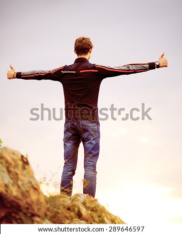 Young Man Standing on the Mountain Peak with Arms Raised. Active Lifestyle Concept.