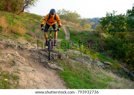 Cyclist in Orange Riding the Mountain Bike on the Autumn Rocky Enduro Trail. Extreme Sport and Enduro Biking Concept.