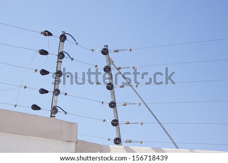 Closeup of electric fence instalation on boundary wall against blue sky