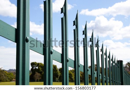 Closeup of green steel palisade security fence against blue sky and clouds
