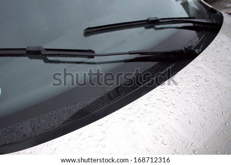An abstract section of the front end of a silver vehicle and its front windscreen bonnet and wipers