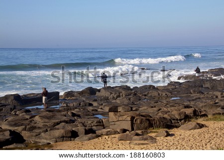DURBAN, SOUTH AFRICA - APRIL 19, 2014: Three unknown fisherman fish from rocks on Ballito beach in Durban South Africa