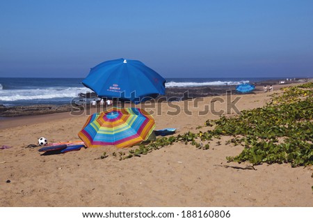 DURBAN, SOUTH AFRICA - APRIL 19, 2014: Numerous unknown people with colorful umbrellas and sporting equipment on Sheffield beach in Durban South Africa