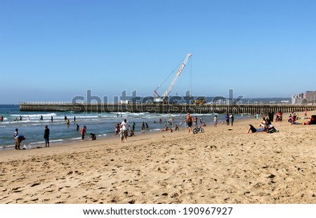 DURBAN, SOUTH AFRICA - MAY 3, 2014: Many unknown people enjoy sunny day on beach while new pier is constructed in background  in Durban South Africa