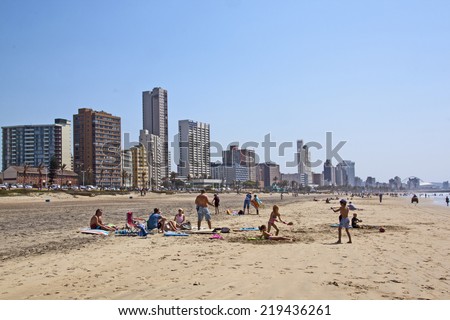 DURBAN, SOUTH AFRICA - SEPTEMBER 21, 2014: Many unknown people enjoy early morning sunshine at beach against city sky line in Durban, South Africa