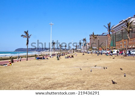 DURBAN, SOUTH AFRICA - SEPTEMBER 21, 2014: Many unknown people and pidgeons relax on grass verge on beachfront in Durban, South Africa