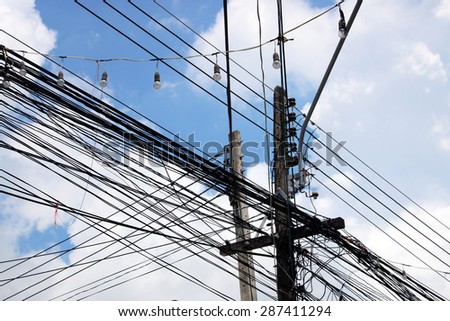 tangled web of cables connected to power supply on wooden pole