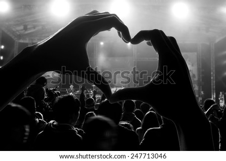 a crowd of people at during a concert with a heart shaped hand shadow