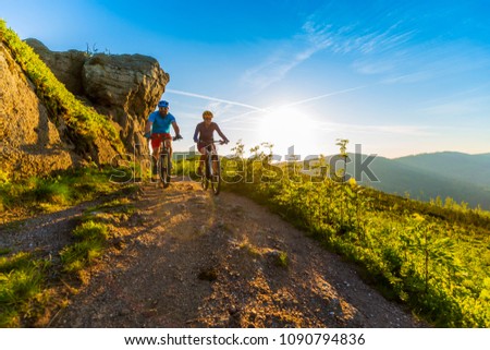 Cycling women and man riding on bikes at sunset mountains forest landscape. Couple cycling MTB enduro flow trail track. Outdoor sport activity.
