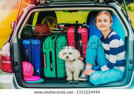 Summer vacation, young girl in car trunk with dog in the car is ready for travel for family vacation.