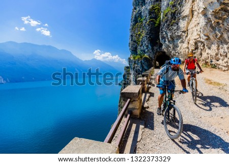 Cycling woman and man riding on bikes at sunrise mountains and Garda lake landscape. Couple cycling MTB enduro flow sentiero ponale trail track. Outdoor sport activity.