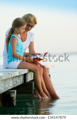 Summer relax, girl with mother reading a book on the pier