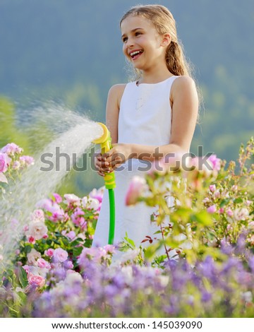 Summer garden, watering - beautiful  girl watering roses with garden hose in the garden