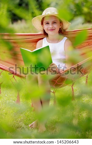 Summer joy, hammock - cute girl reading a book  in a hammock in the garden