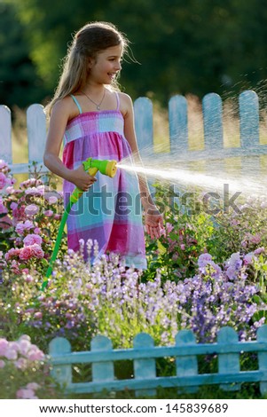 Watering, flower garden - beautiful girl watering roses with garden hose in the garden