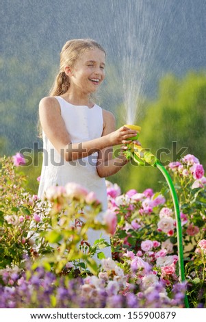 Summer garden, watering - beautiful  girl watering roses with garden hose in the garden
