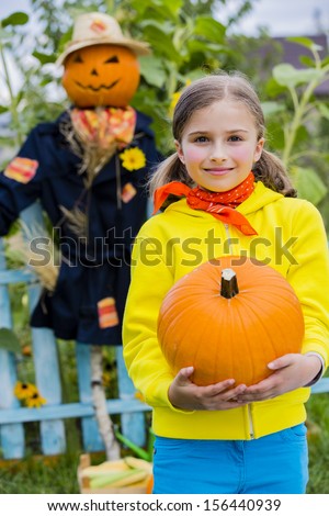 Autumn harvest - Scarecrow and happy girl  in the garden