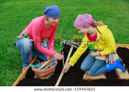 Gardening, sowing seeds to the soil -  girl helping mother in the garden