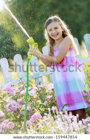 Summer fun, watering flowers - lovely girl has fun watering flowers in the garden