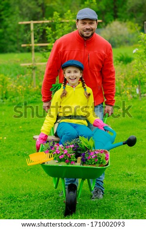 Gardening, planting - girl in barrow helping father in the garden