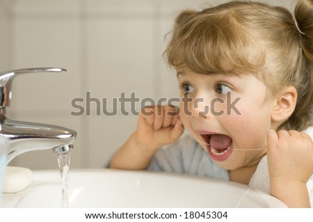 Cute girl cleaning teeth by floss in bathroom