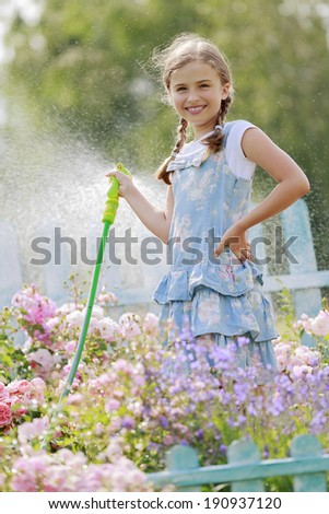 Garden and summer fun - beautiful girl watering roses with garden hose in the garden