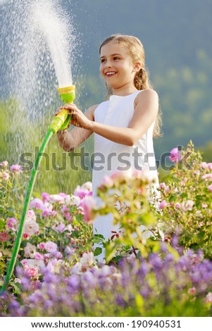 Summer garden, watering -  girl has fun watering roses with garden hose