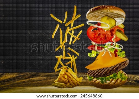 Delicious french fries and cheeseburger stacked high with a juicy beef patty, cheese, fresh lettuce, onion and tomato with flying ingredients and copyspace
